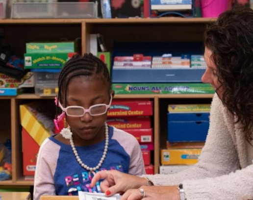 A visually impaired student with her teacher. She is dark skinned and wearing glasses.