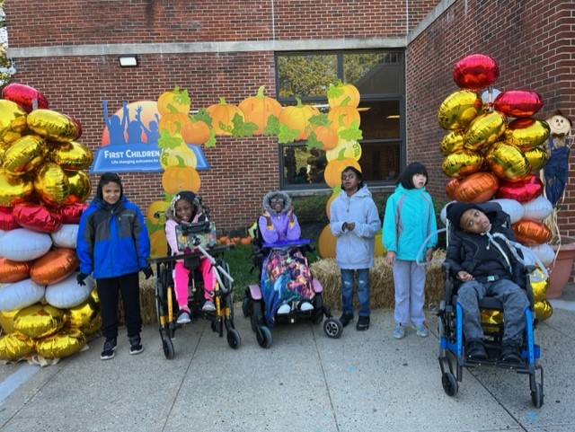 A group of students stands in front of a balloon arch. They are outside.